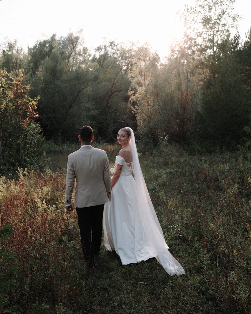 Bride looks back walking through the vineyard with groom