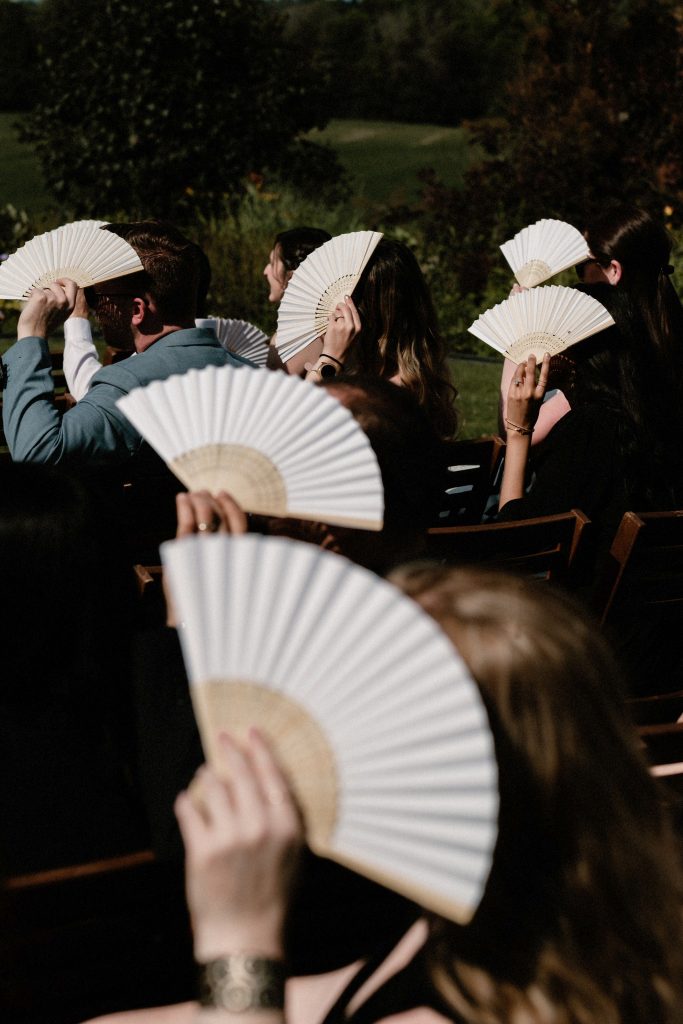 guests fan from sun outside at ceremony